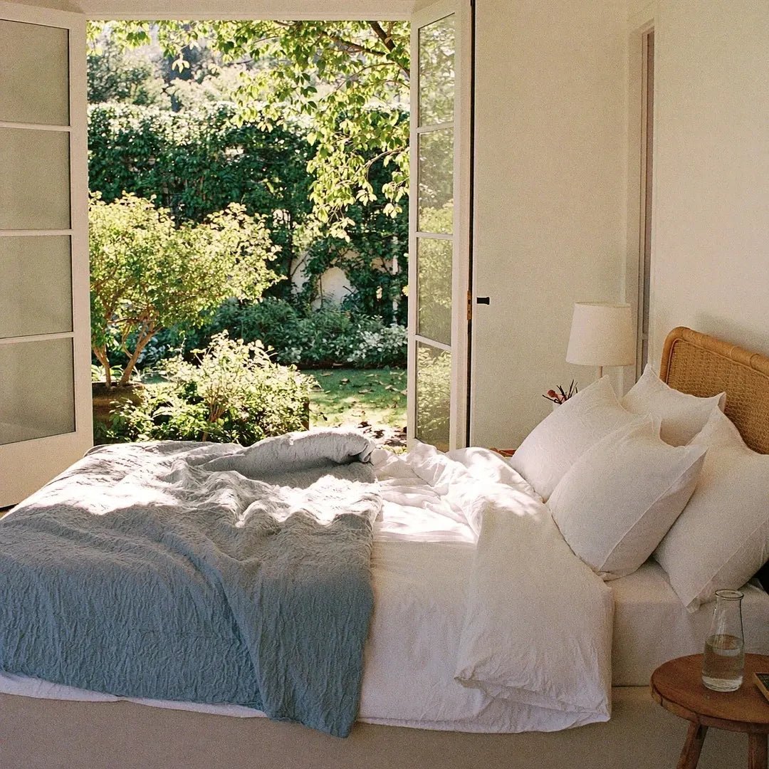 Bedroom with a large bed, white pillows, and a view of greenery outside.