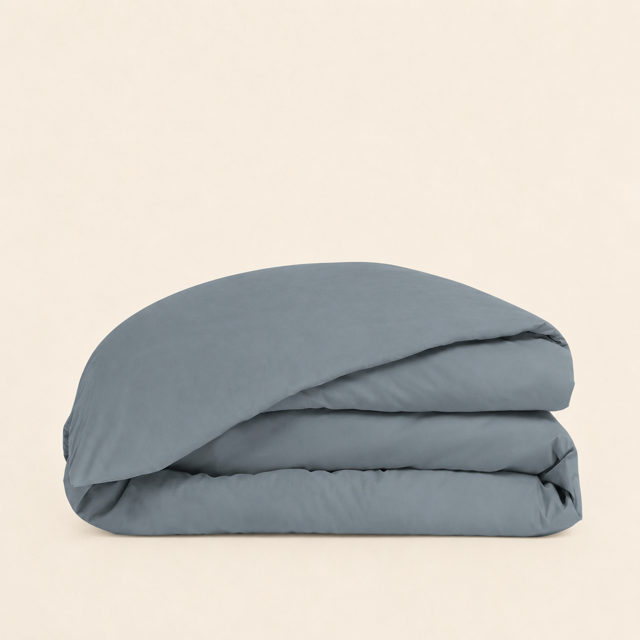 A folded dusty blue bedding item, likely a duvet cover or comforter, stacked neatly on a solid, warm off-white background.